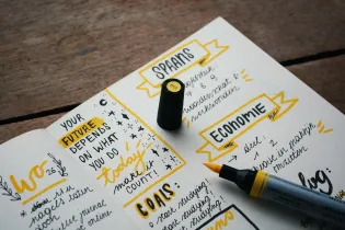 A white notepad with a yellow and black highlighter with a wooden background. Written in this notepad are the words: 'Your future depends on what you do today. Make it count'.