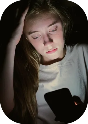 Blonde female teenager staring at her phone in the dark. The phone is illuminating her face.