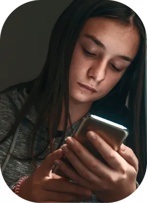 Brunette teenage girl staring at her phone in the dark. The phone is illuminating her face.