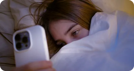 Teenage girl lying in bed using smartphone in dark room