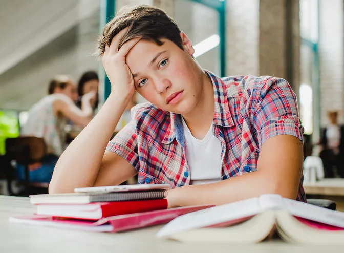 Exhausted teenager with hyperactive ADHD sitting at desk looking overwhelmed