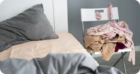 A messy room with an unmade bed and clothes piled up on a chair