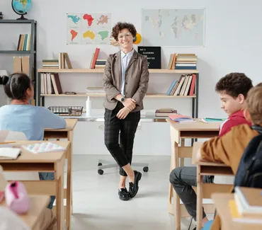 A teacher standing in front of a classroom, engaging with students sitting at their desks.