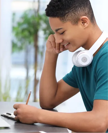 Teenage boy with headphones writing on an exam pad.