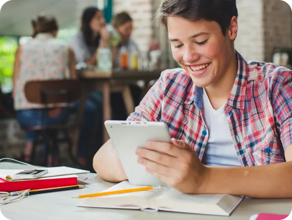 A smiling student working on a tablet at a desk with books and notebooks, promoting Coachbit's partnership program for boosting student success through customized coaching programs.