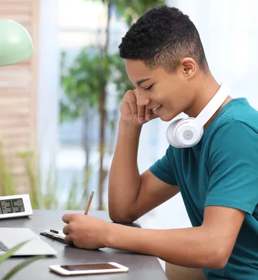 Teenage boy with headphones writing on an exam pad.