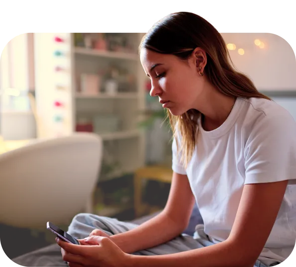 Hopeless teenage girl sitting on her bed staring at her phone.