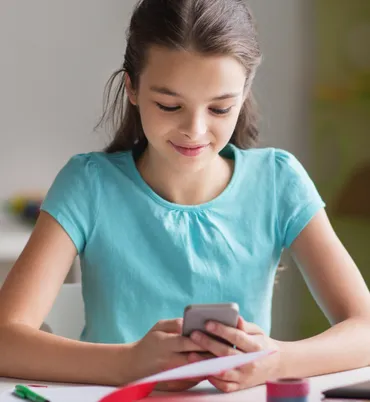 Brunette teenage girl with teal blouse holding her phone and smiling. She is talking to her coach via the Coachbit Application.