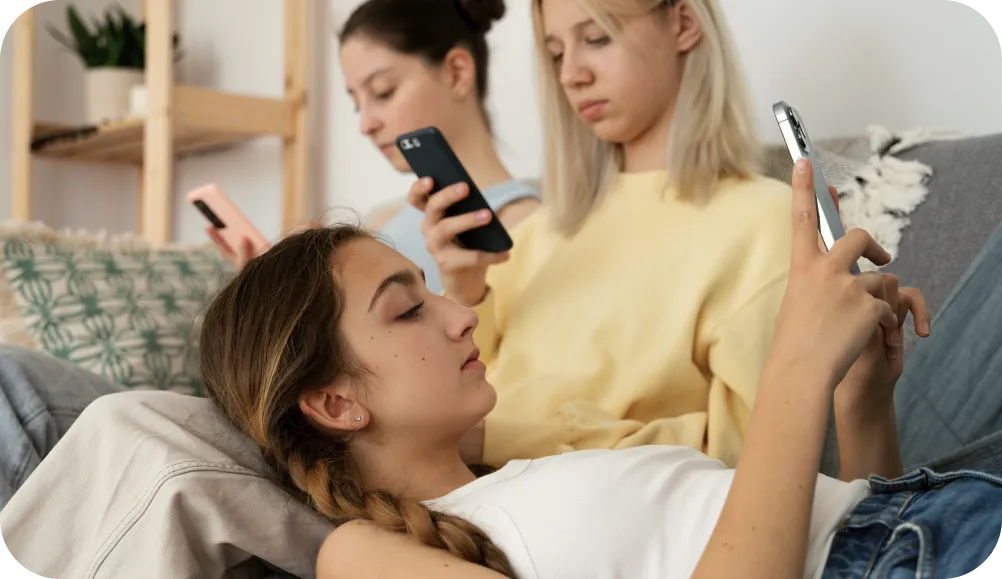 Three teenage girls sitting on the coach and staring at their phones.