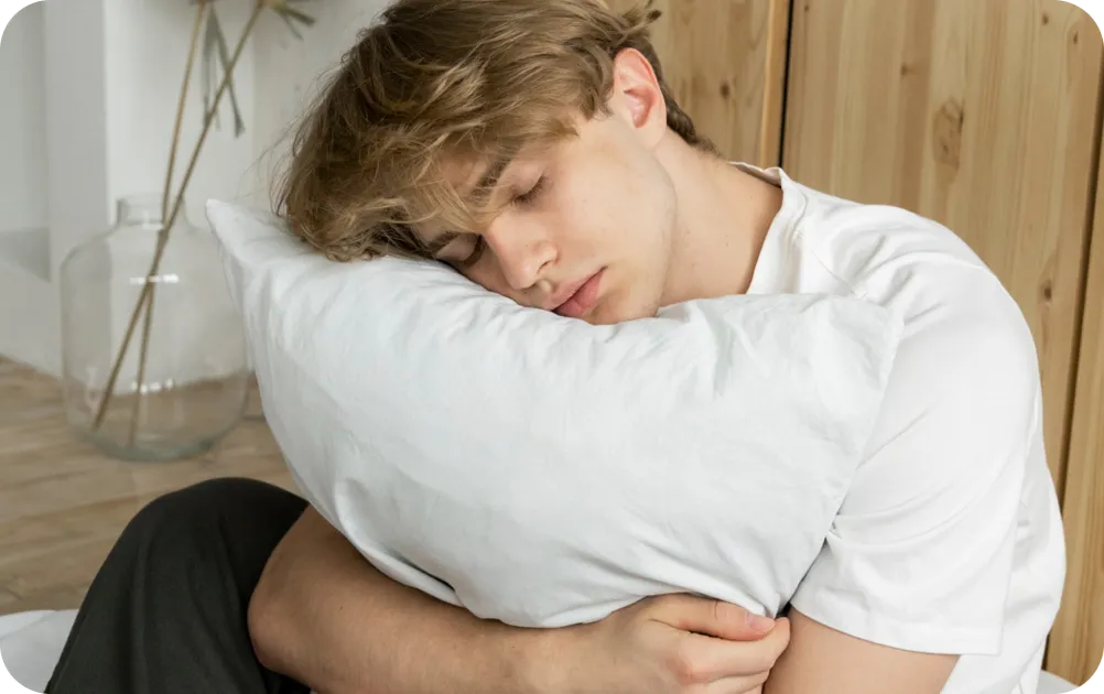 Teenage boy sitting on the floor hugging a pillow, fast asleep.