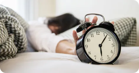 Alarm clock with a person in bed reaching over to hit snooze